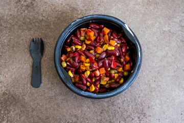beans,corn,peas and carrots in black plastic bowl on brown background