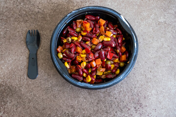 beans,corn,peas and carrots in black plastic bowl on brown background