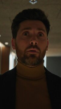 Portrait of young Caucasian man feeling dizzy while walking down hallway, holding onto wall. Businessman in formal clothes leaning on wall in hotel. Shot on camera with anamorphic lens
