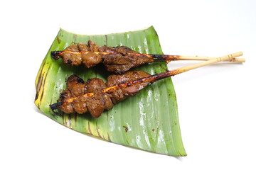 Dark brown roasted Chicken livers Thai style on bamboo skewer put on banana leaf with white background.