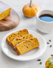 Pumpkin sweet bread or cake with icing on a plate on a light background with decorative pumpkins and a cup of coffee close up.