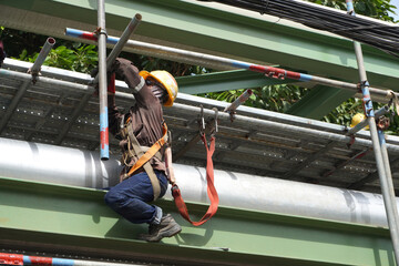 The workers are installing scaffolding at a height to support the construction of product pipelines in the gas and oil industrial estate area