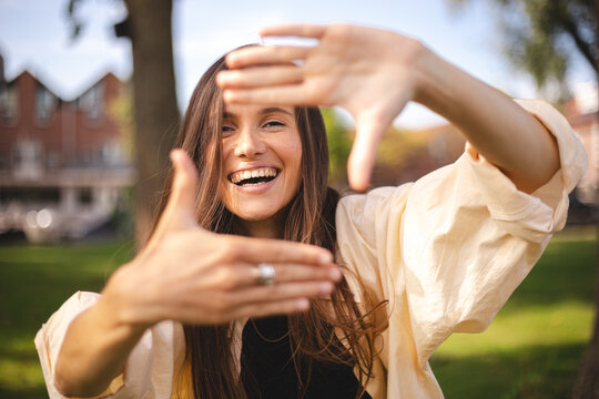 Attractive cheerful brunette girl having fun showing frame capture good mood rest vacation outdoors. Girl looking for the frame making a square with her fingers and looking through. 