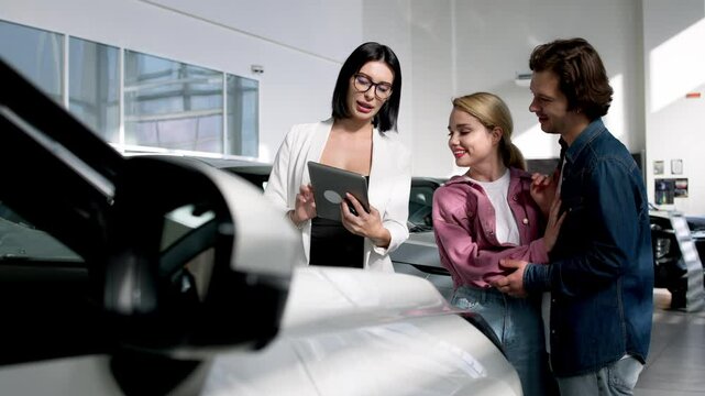 A married couple consults with a female dealer in a modern showroom about their options for a luxury car. This interaction showcases personalized service and expertise in the car-buying experience.