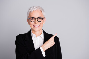 Photo portrait of pretty senior female professional entrepreneur point empty space wear formalwear specs isolated on gray color background
