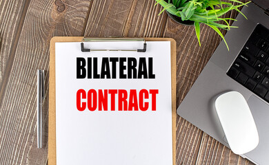Business concept with bilateral contract message on clipboard, laptop, pen, and plant on desk