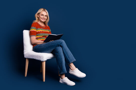 Photo of charming nice woman wear stylish clothes sit chair read book empty space isolated on dark blue color background