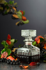 Black chokeberry juice or liquor and fresh berries on a black background.