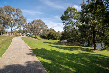 A concrete footpath or cycling trail along Werribee river with large open green space and some suburban houses in the distance. Beautiful and clean environment in neighborhood of Melbourne Australia.