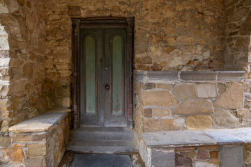 A weathered wooden door with a greenish tint showcases decorative panels, within a charming stone archway. Rustic charm of an old European village.