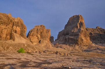 Majestic peaks illuminated by sunset rays stand out around rifugio Alimonta. A tent in foreground....