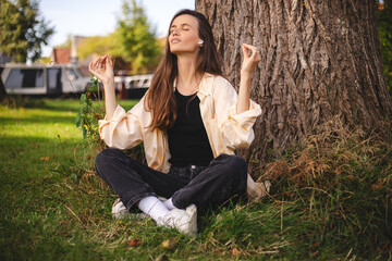 Young woman in lotus flower position sitting with her eyes closed in park, she is meditating...