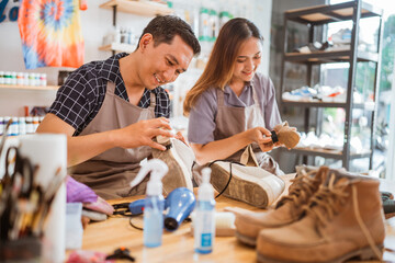 male worker polishing footwear in shoes laundry workshop helped by co worker
