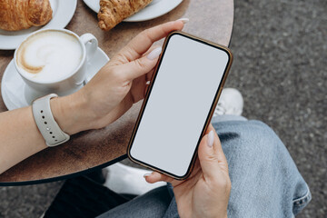 Mockup woman's hand holding using smart phone with white blank screen POV at coffee shop, mobile...