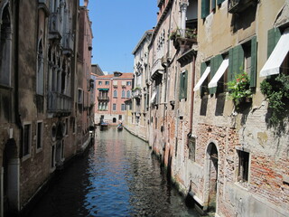 Scenic Venetian cityscape with narrow canal on a sunny summer day. Romantic Venetian landscape. Tourists in a gondola on a walk along a Grand Canal in the old town. Famous historical heritage city.