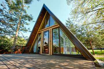 Modern A-frame cabin nestled among trees in a serene outdoor setting during sunny daylight