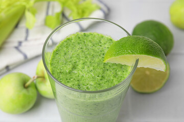 Tasty green smoothie in glass with lime and apples on light table, closeup