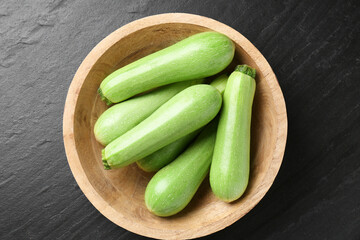 Fresh zucchinis in bowl on dark textured table, top view