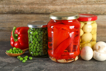 Different pickled products in jars on grey textured table