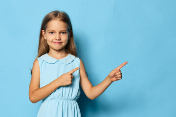 Curious little girl in blue dress pointing upward against a matching blue background