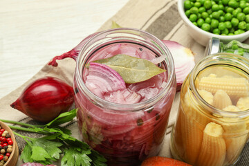 Different pickled products in jars and fresh ingredients on white table