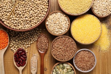 Different types of legumes, seeds and cereals on wooden table, flat lay