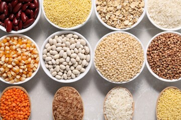 Different types of legumes and cereals on light marble table, flat lay