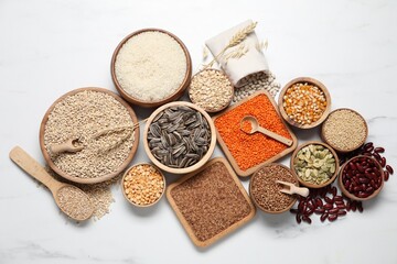 Different types of legumes, seeds and cereals on white marble table, flat lay