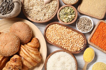 Different types of cereals, seeds, bread and legumes on white wooden table, flat lay