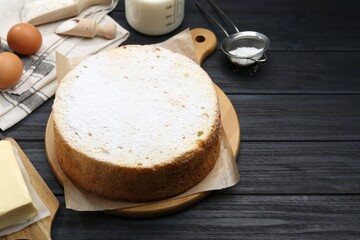 Delicious sponge cake and ingredients on black wooden table