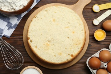 Delicious cut sponge cake, whisk and ingredients on wooden table, flat lay