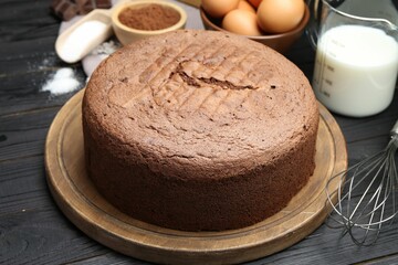 Tasty chocolate sponge cake and ingredients on black wooden table, closeup