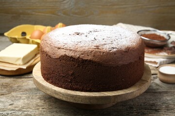 Tasty chocolate sponge cake with powdered sugar and ingredients on wooden table, closeup