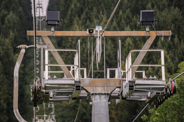 Close-up of a ski lift mechanism with pulleys and cables in a forested mountain area, showing industrial details against a natural backdrop..