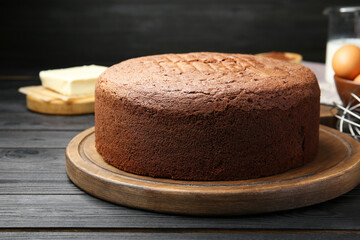 Tasty chocolate sponge cake and ingredients on black wooden table, closeup