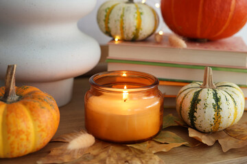 Burning candle, pumpkins and dry leaves on wooden table, closeup. Autumn atmosphere