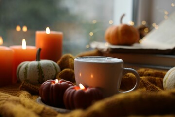 Cup of coffee, pumpkins and burning candles on soft sweater, closeup. Autumn atmosphere