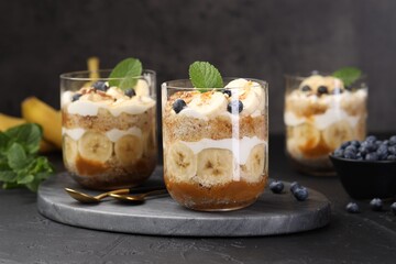 Tasty trifle dessert. Sponge cake, blueberries, banana and whipped cream in glasses on black table