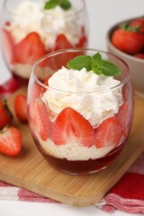 Tasty trifle dessert. Sponge cake, strawberries, jam and whipped cream in glasses on table, closeup