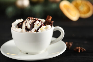 Tasty hot cocoa drink with whipped cream in cup and spices on black table, closeup