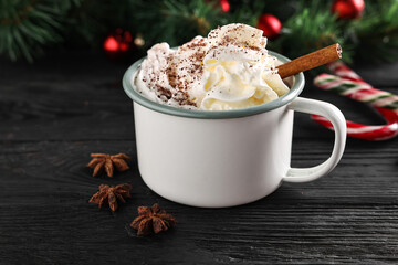 Tasty hot cocoa drink with whipped cream in mug and spices on black wooden table, closeup