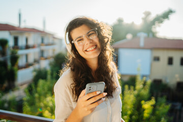 Young caucasian woman listening to music or audio book on her balcony