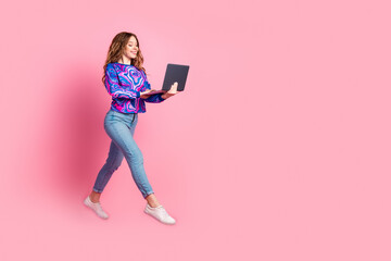 Full size photo of pretty young woman jump run empty space laptop wear pullover isolated on pink color background