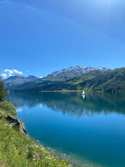 Alpine mountain lake in clear sunny weather in summer. Beautiful view of lake in Swiss mountains on sunny day, contrasting colors, bright light, boat on lake.