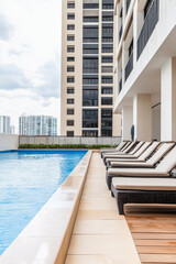 Fototapeta premium Luxurious swimming pool area with lounge chairs overlooking a city skyline on a cloudy day