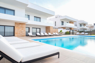 Fototapeta premium Modern residential poolside area with loungers and contemporary architecture on a sunny day