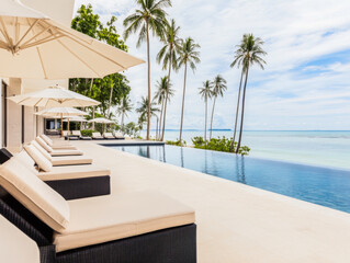 Obraz premium Luxurious poolside lounge chairs with umbrellas overlooking the tranquil sea at a tropical resort on a sunny day