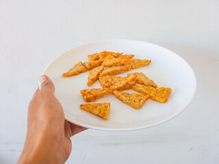 female hand holding a plate of fried tempeh isolate on white