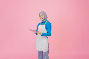 A cheerful and happy woman is wearing a blue shirt along with an apron while using a tablet