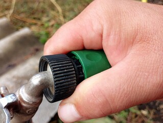 A person manually connects a water supply hose to a water tap using a plastic green connection.